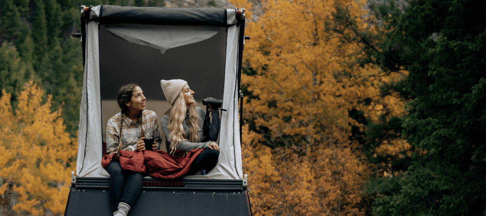 two girls looking out of a roof top tent during fall foliage