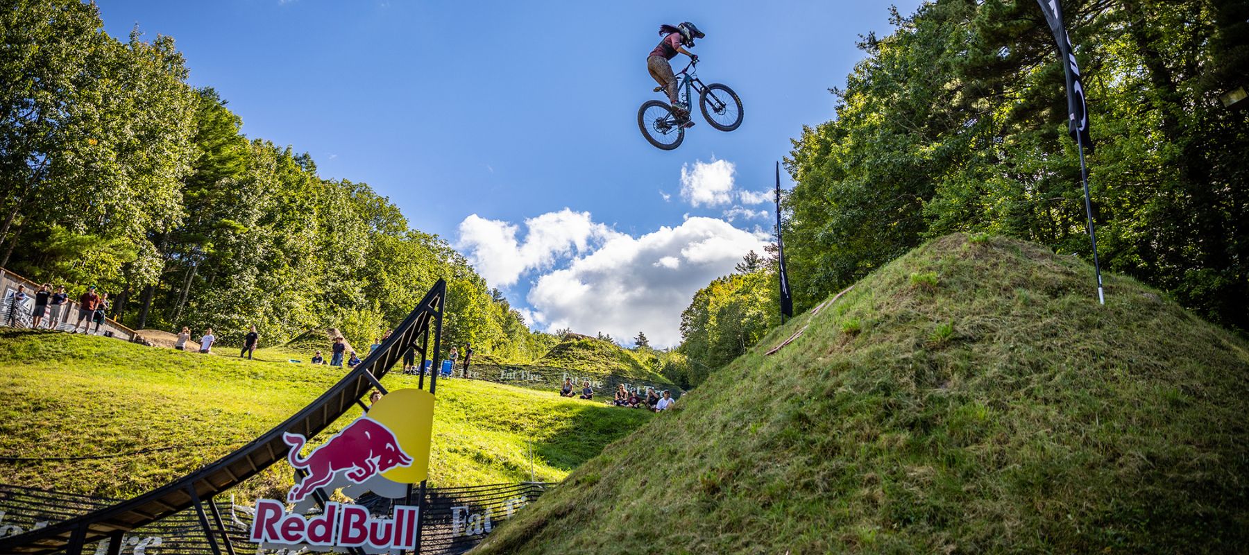 Kajay Rooke launching off a bike ramp with forest scenery in the background