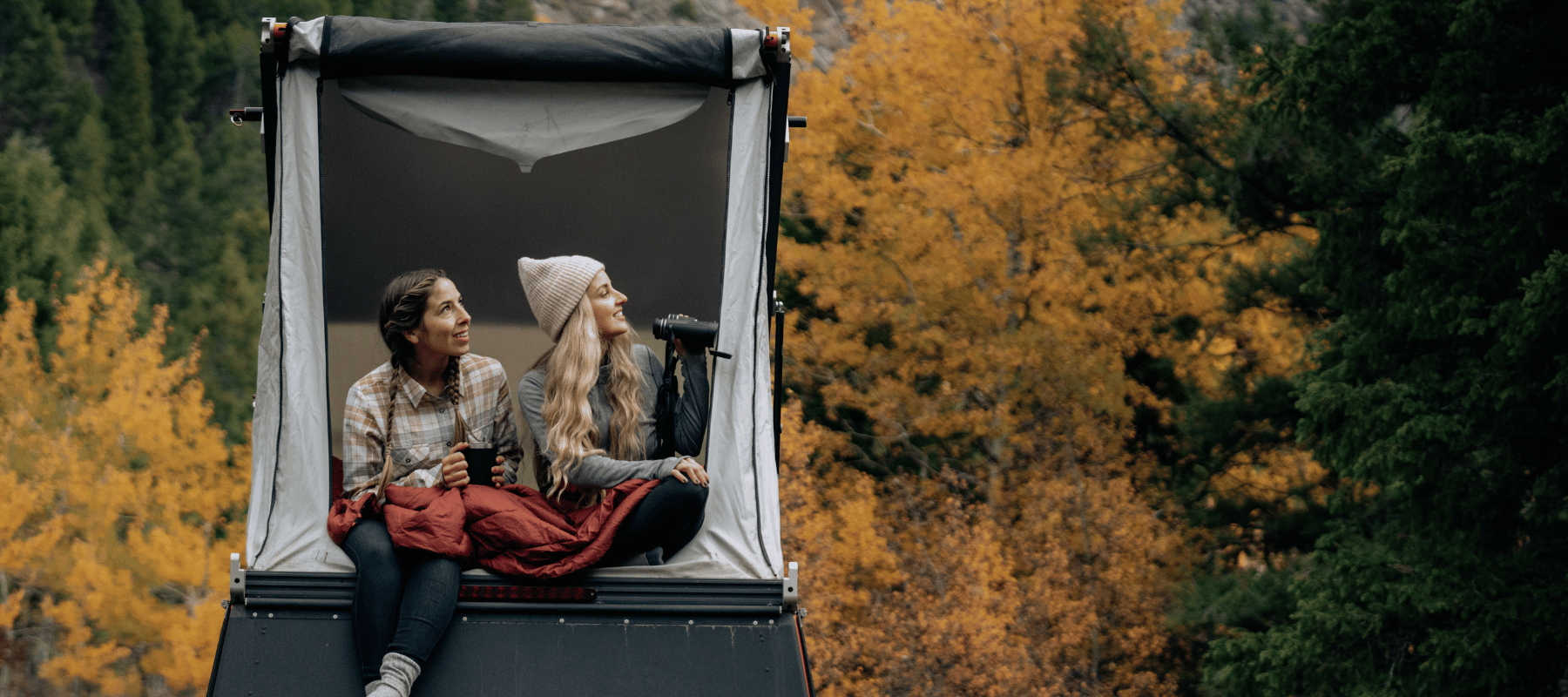 two girls looking out of a roof top tent during fall foliage 