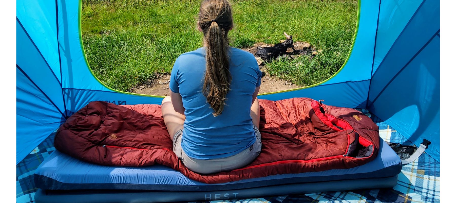 photo of someone sitting on HEST Sleep System in tent overlooking green pasture while camping
