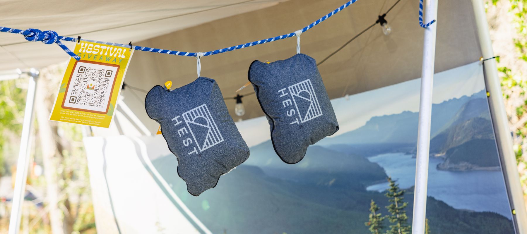 HEST pillows hanging from rope in tent in front of scenic poster overlooking water and mountains