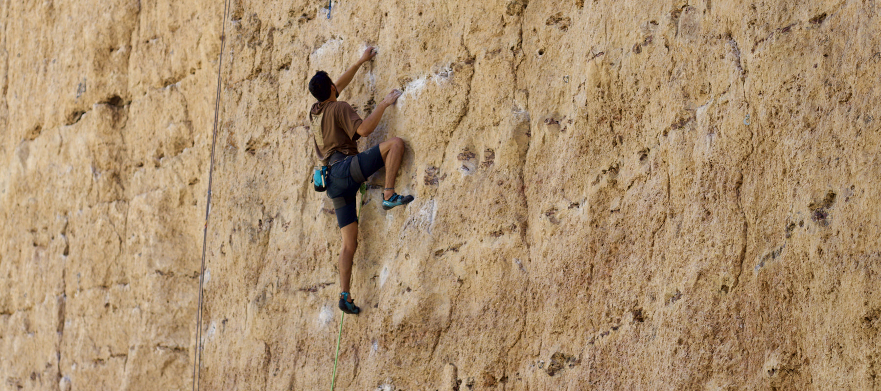 This photograph shows a person climbing on an sheer rock face. They are using ropes and the climber is reaching upward. R
